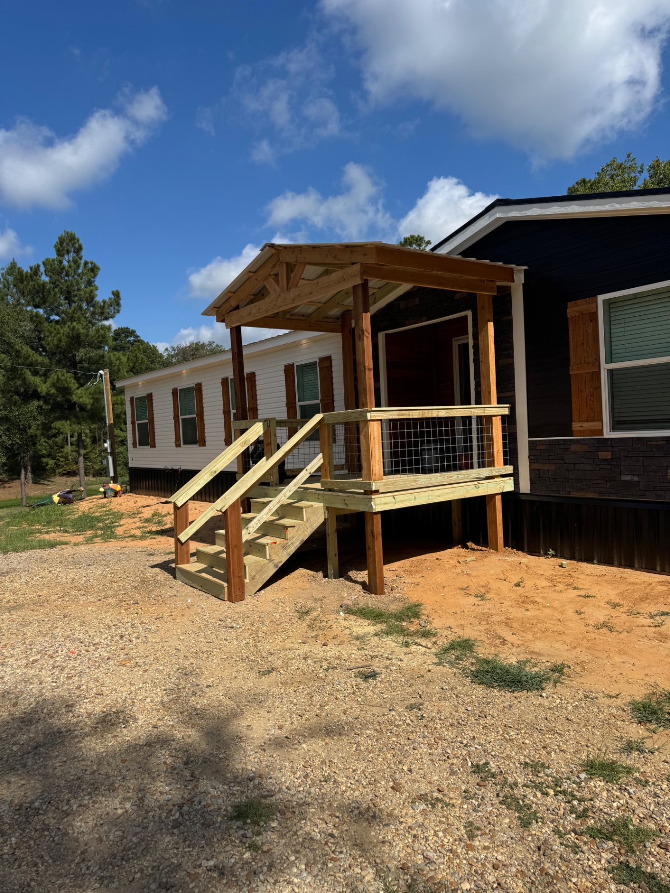 Covered gable-roof entry porch with wire mesh railing and stairs on a mobile home